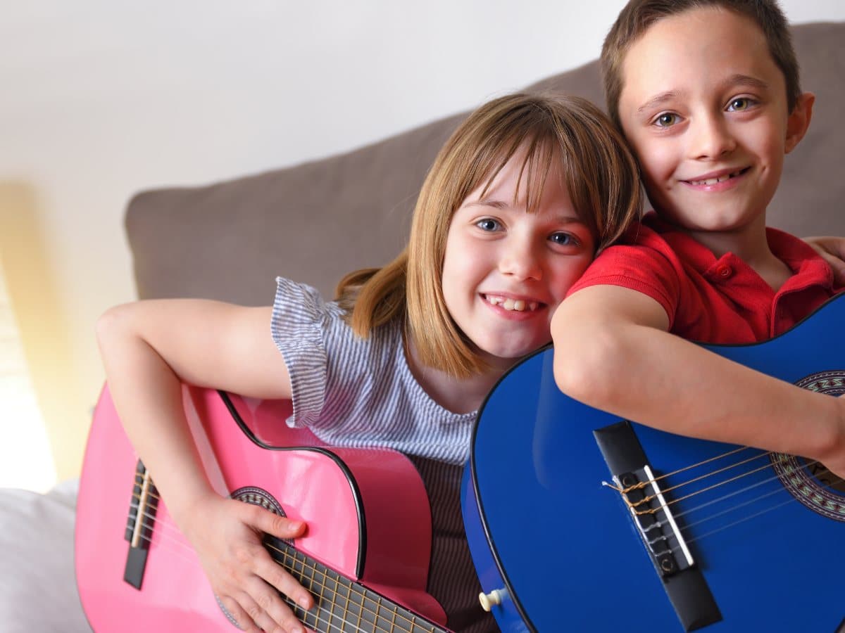 A girl and a boy smiling together holding guitars during a group lesson at Melody Magic